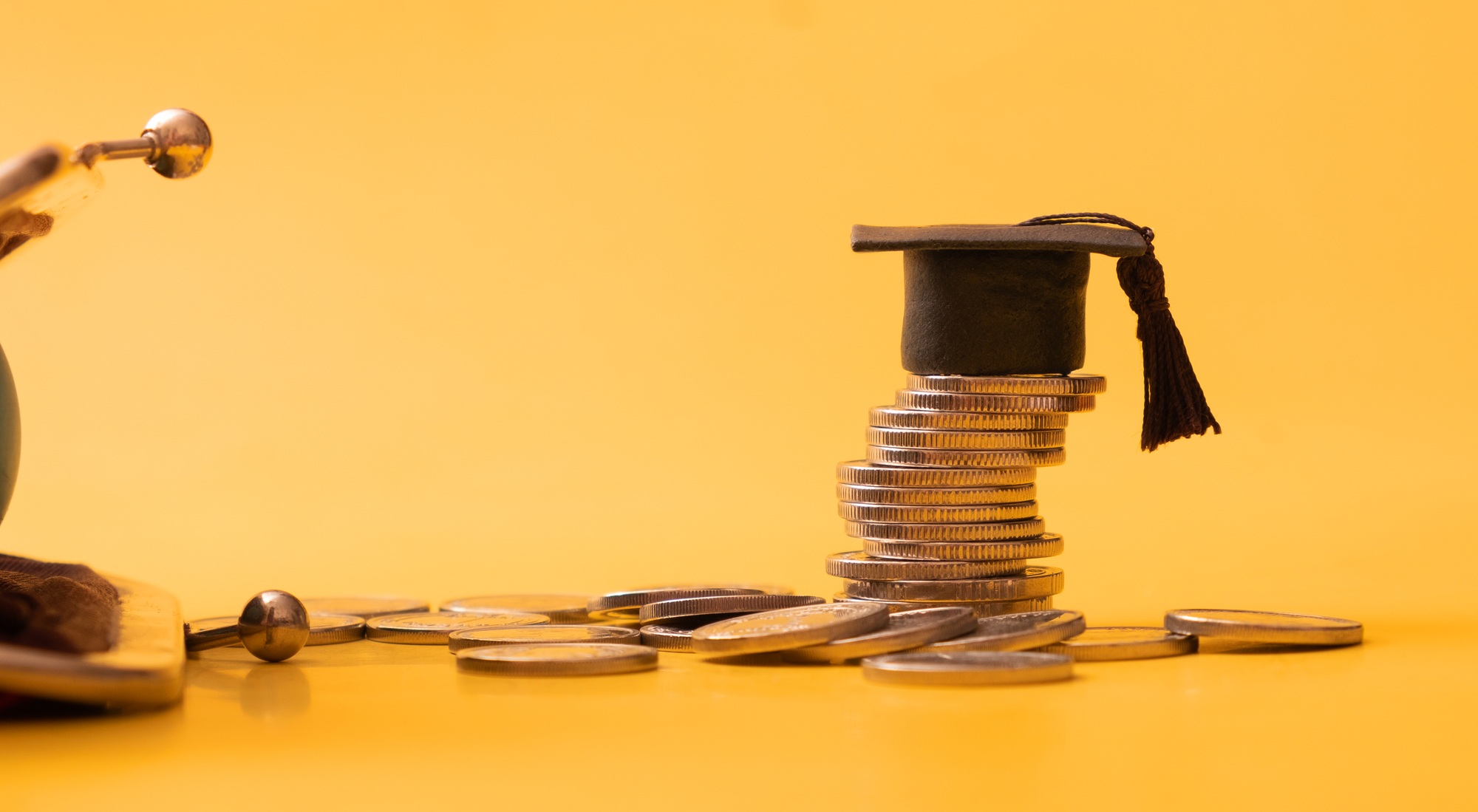 Graduated cap with coins and wallet fragment on orange background. Financial literacy concept