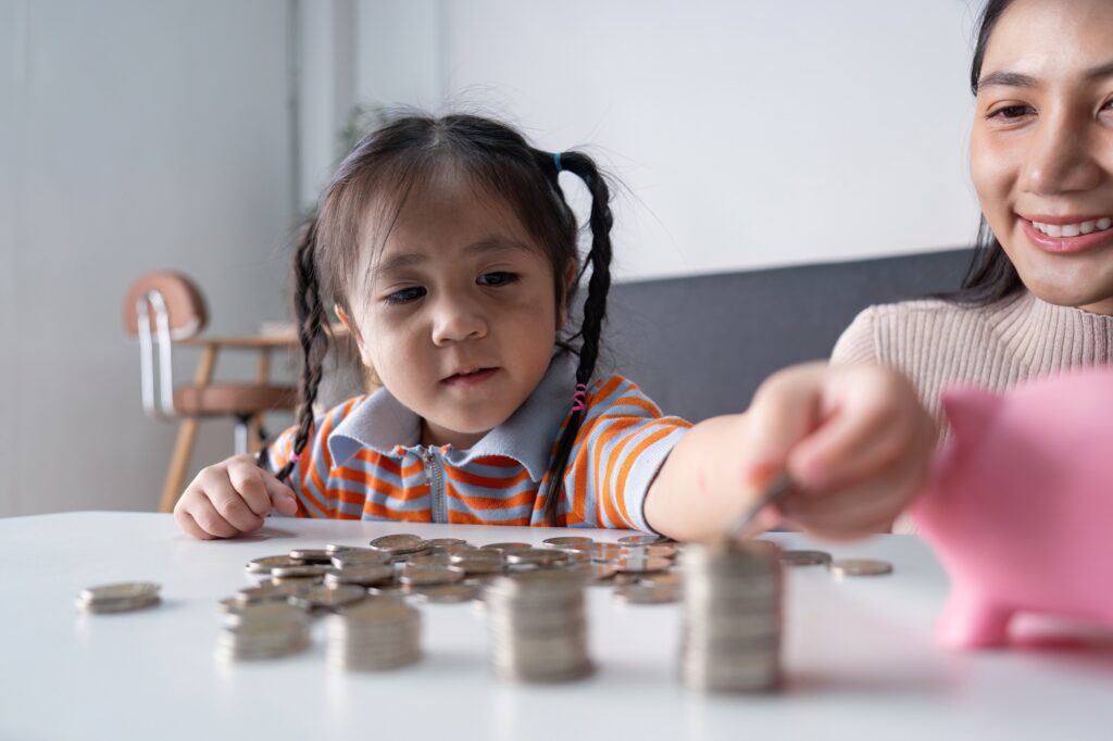 Mother Teaching Daughter Financial Literacy with Coins and Piggy Bank
